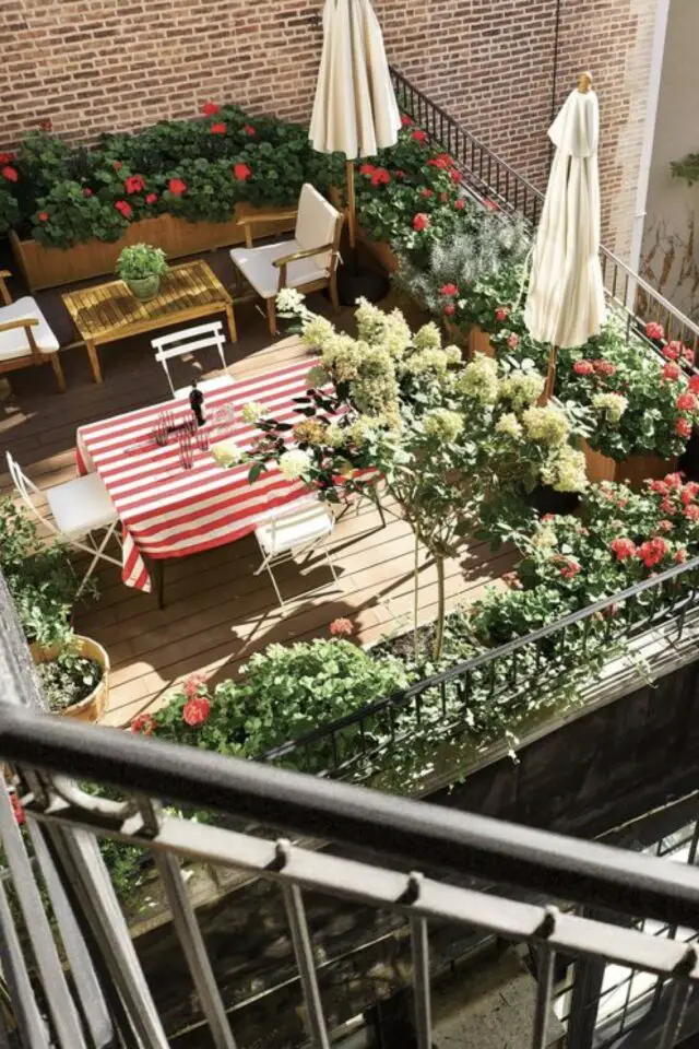 amenagement terrasse appartement ville Table de repas nappe rayée blanche et rouge parasol blanc ombre plantes en pots fleurs et arbuste 
