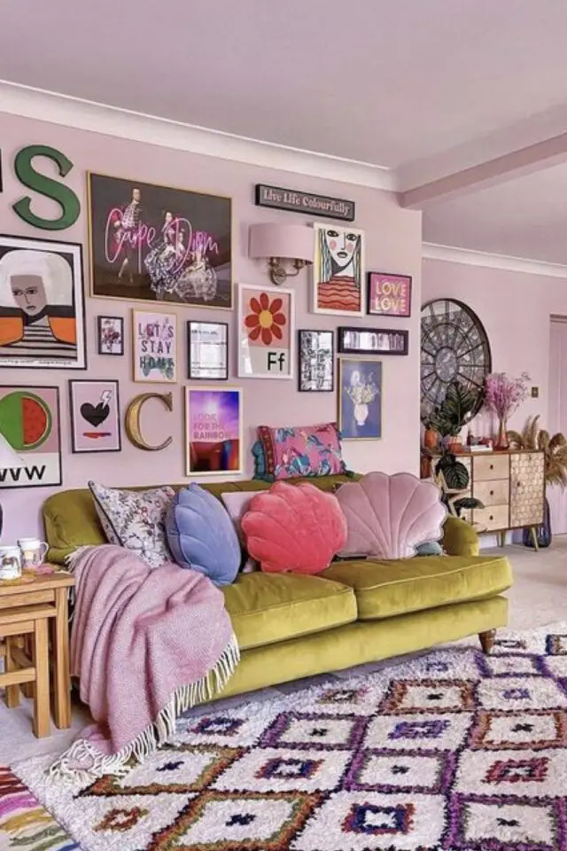caractéristique décoration maximaliste mur rose clair salon séjour canapé velours vert galerie de cadres affiches coussins coquillage colorés 