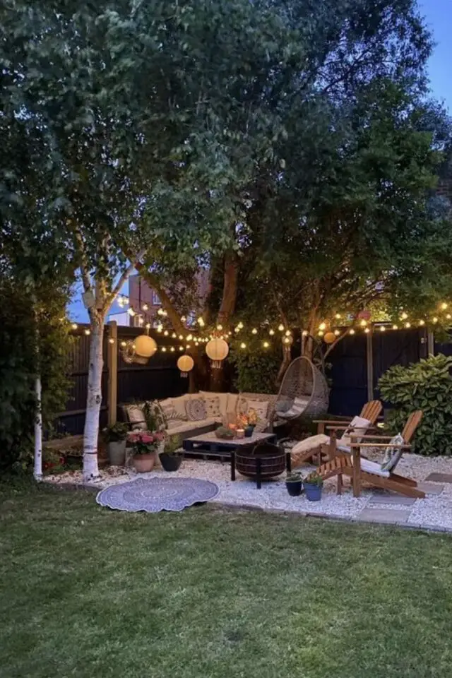 conseils tout savoir sur le mobilier de jardin coin lounge canapé fauteuil transat en bois guirlande lumineuse sous les arbres gravier et pelouse 