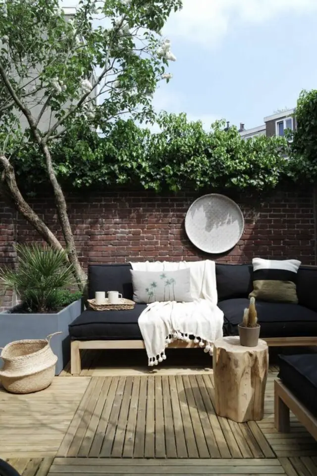 conseils tout savoir sur le mobilier de jardin maison de ville terrasse en bois mur en brique canapé en bois et coussin noir verdure végétation 