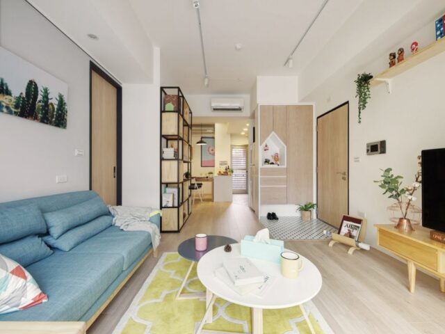 petite maison simple et colorée porte entrée donnant sur le salon canapé bleu tapis jaune meuble en bois bibliothèque vestiaire sur mesure 
