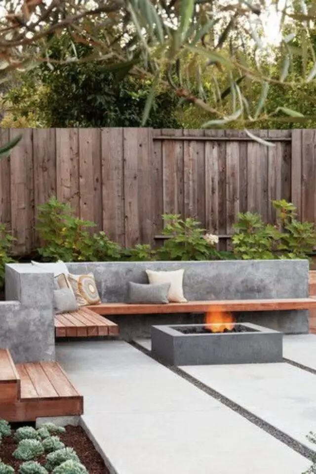 terrasse moderne en béton exemple grande dalle brasero banquette assise en bois aménagement élégant massif de fleur et de plantes clôture en bois 
