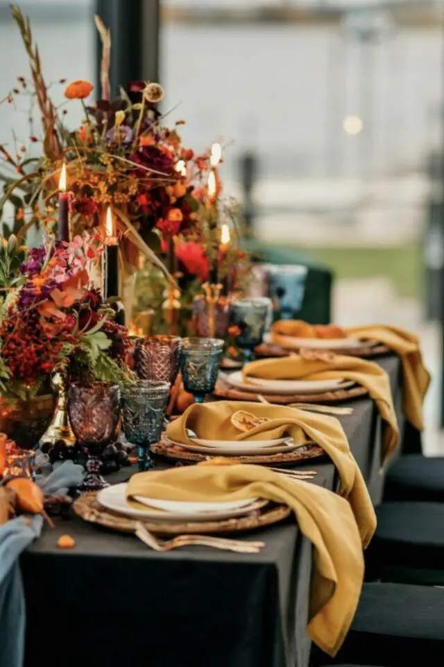 idée déco mariage automne décor de table élégant coloré serviette en tissu jaune bouquet de fleur orangé et rouge bougie noires verre à pied en verre fumé 