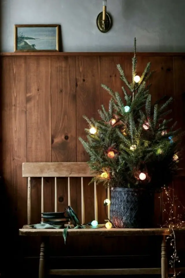 petit sapin de noël exemple décoration banc vintage en bois mur en lambris naturel panier tressé noir guirlande lumineuse 